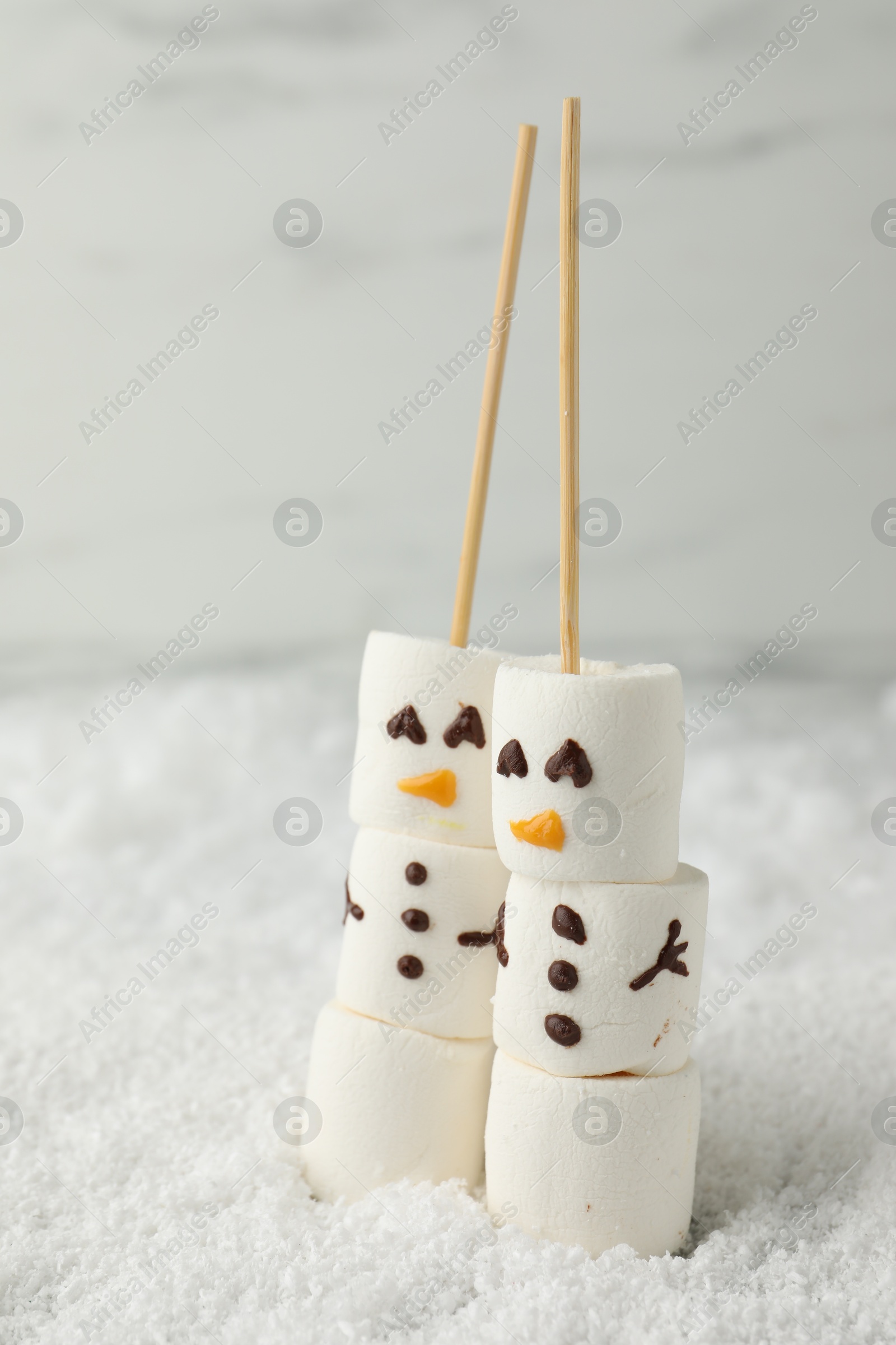 Photo of Cute snowmen made of marshmallows on artificial snow