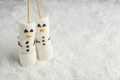 Photo of Cute snowmen made of marshmallows on artificial snow. Space for text