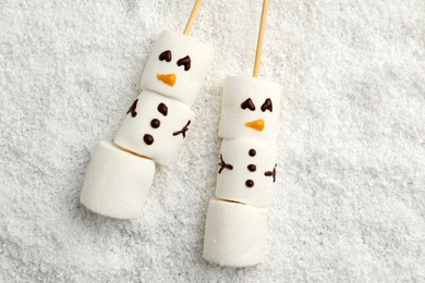 Photo of Cute snowmen made of marshmallows on artificial snow, top view