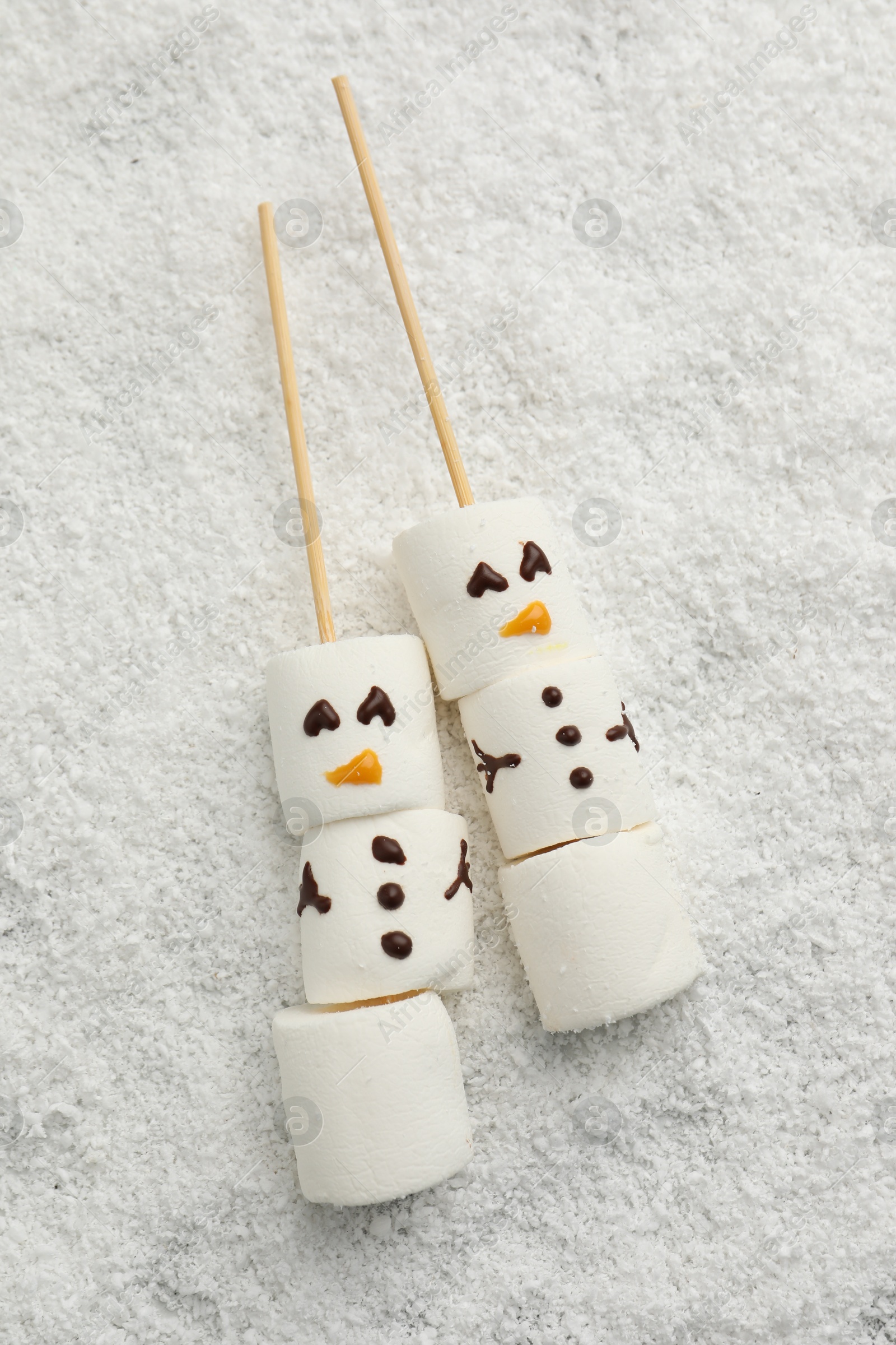 Photo of Cute snowmen made of marshmallows on artificial snow, top view