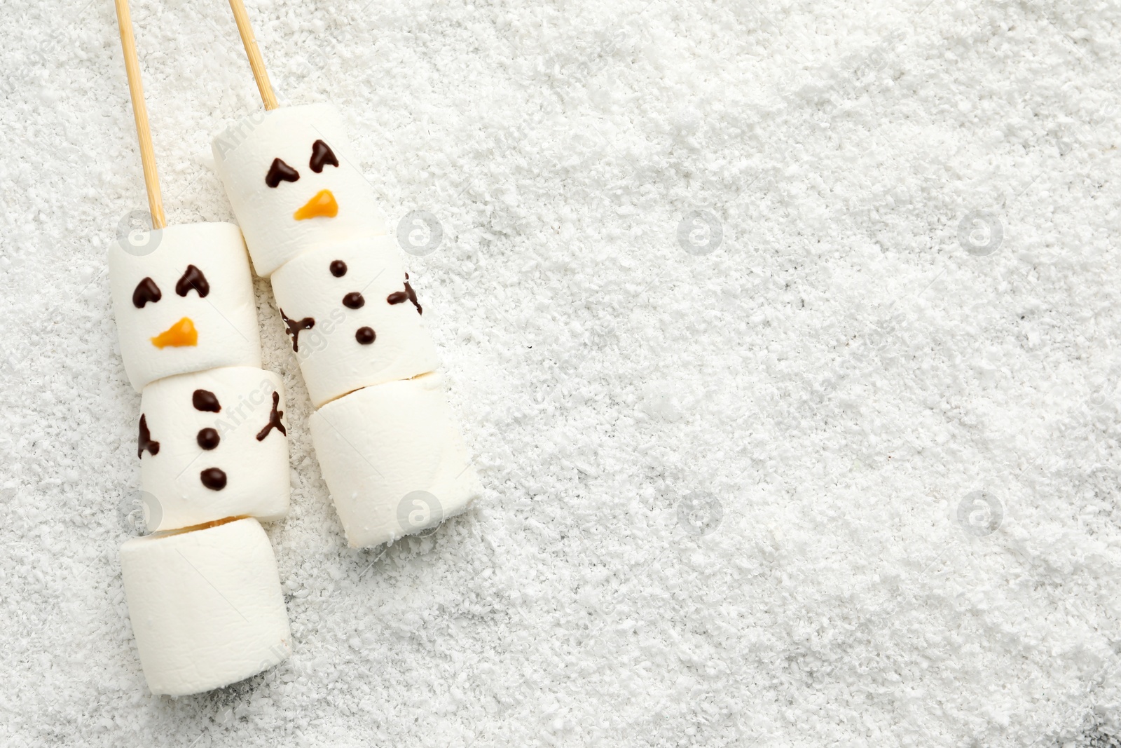 Photo of Cute snowmen made of marshmallows on artificial snow, top view. Space for text