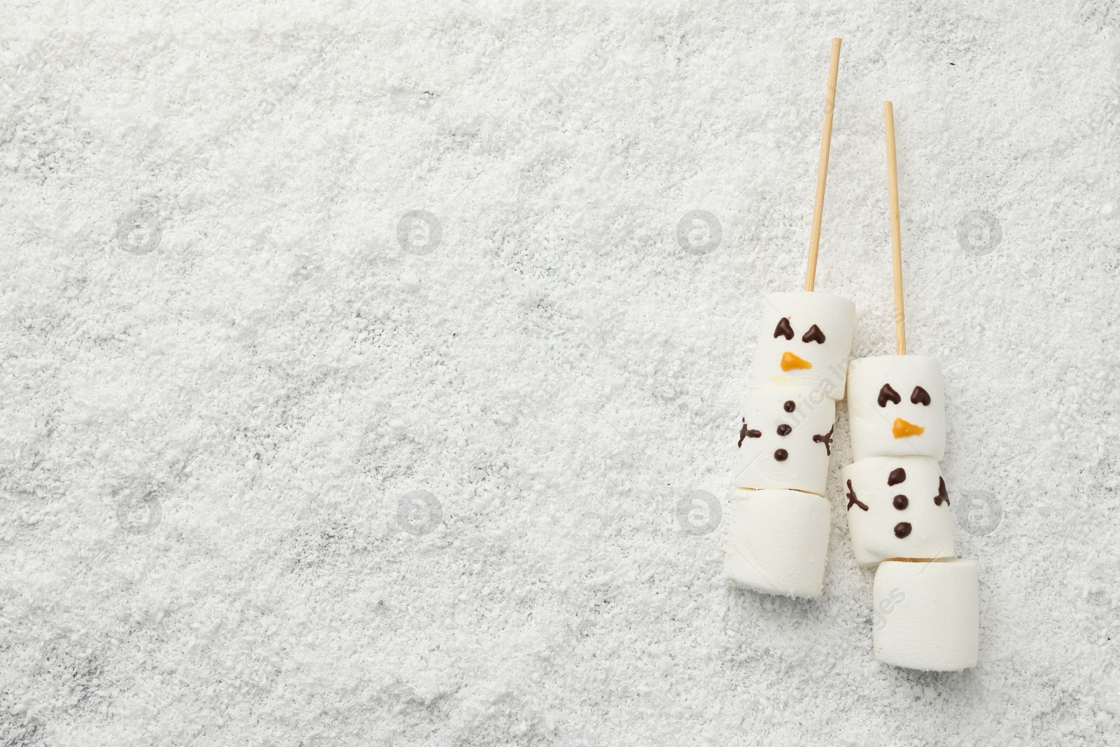 Photo of Cute snowmen made of marshmallows on artificial snow, top view. Space for text