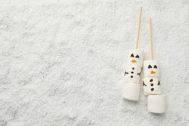 Photo of Cute snowmen made of marshmallows on artificial snow, top view. Space for text