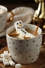 Photo of Cute marshmallow snowman in cup of hot drink on wooden table with Christmas decor, closeup