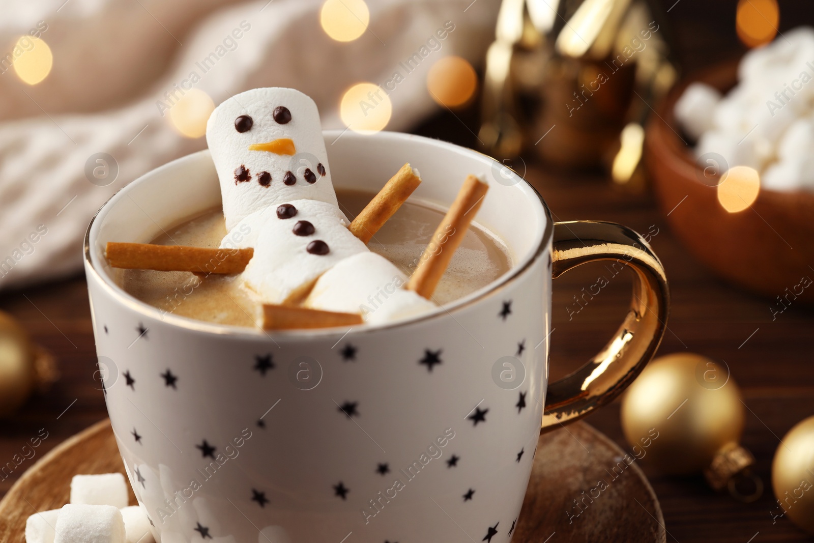 Photo of Cute marshmallow snowman in cup of hot drink on table with Christmas decor, closeup