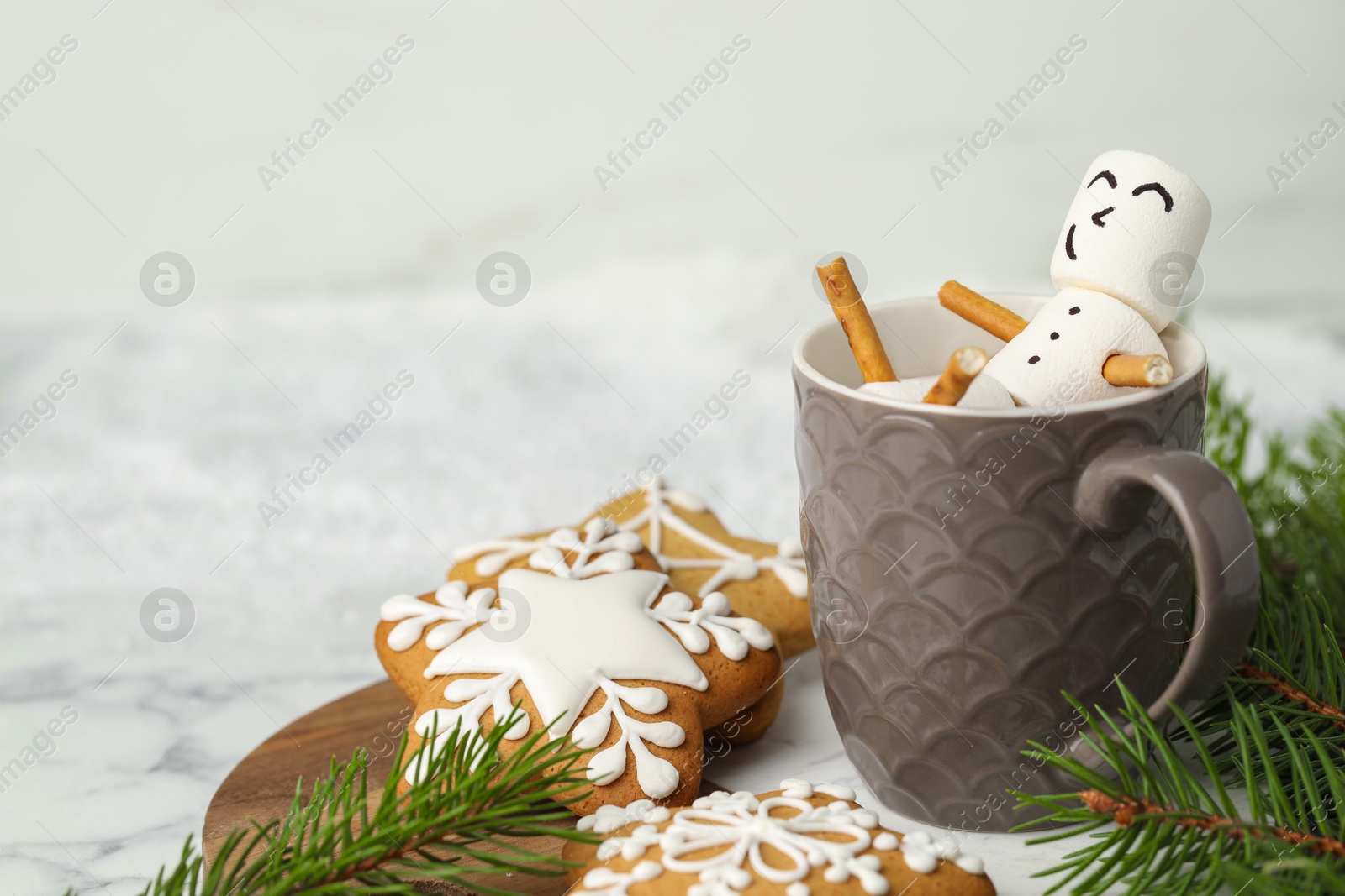 Photo of Cute marshmallow snowman in cup of hot drink and gingerbread cookies on white table with Christmas decor, closeup. Space for text