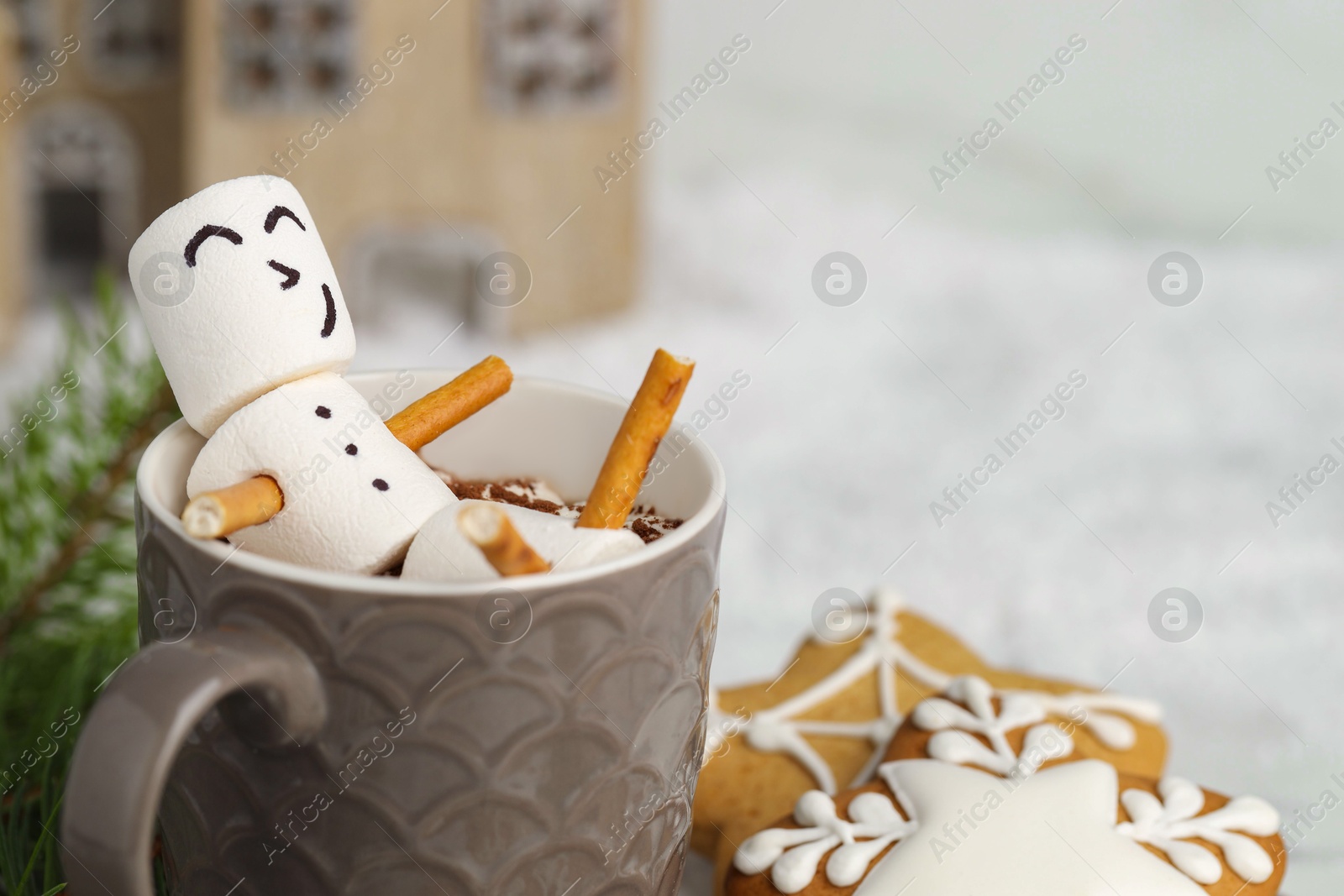 Photo of Cute marshmallow snowman in cup of hot drink and gingerbread cookies on white table with Christmas decor, closeup. Space for text