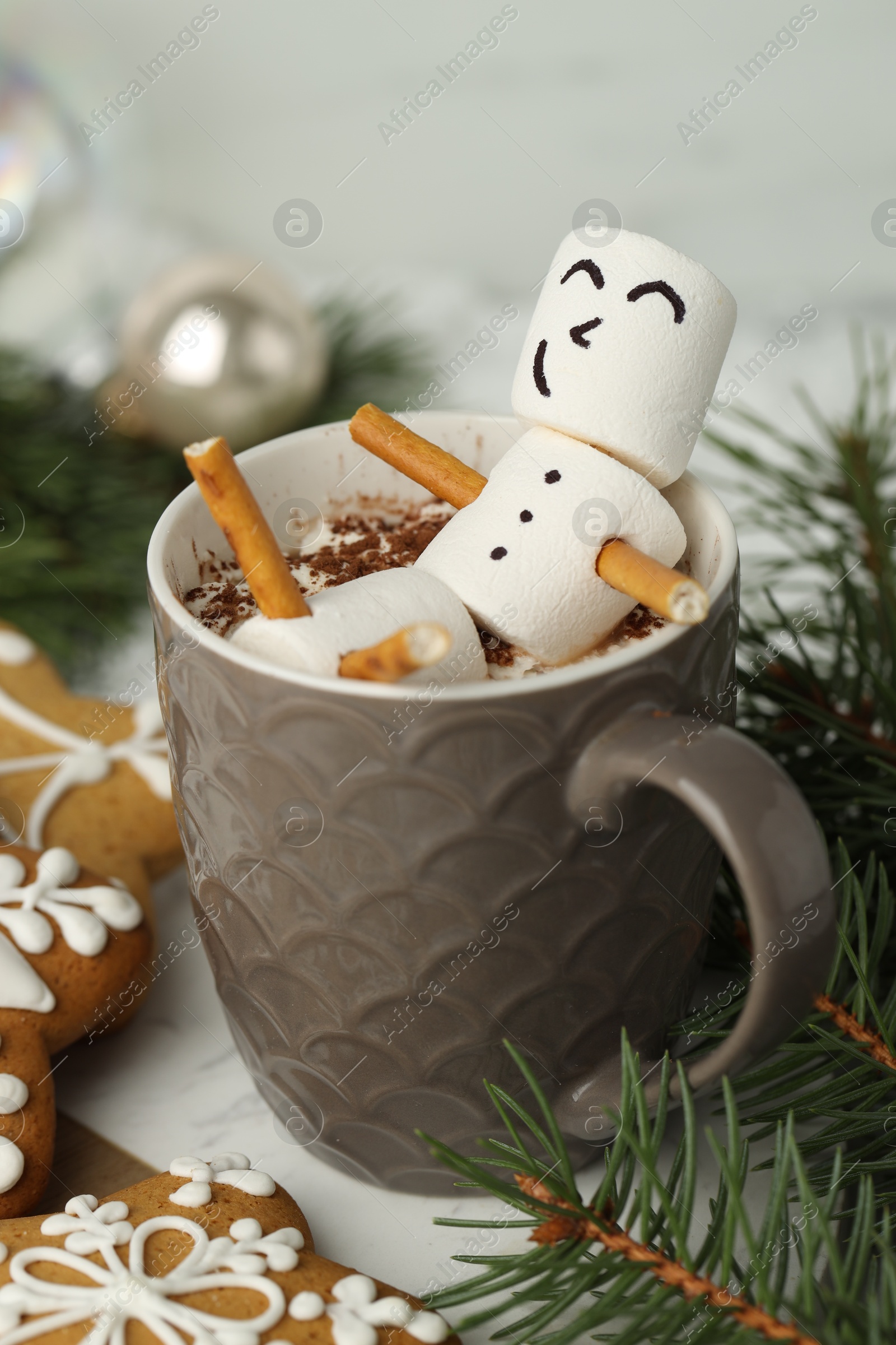 Photo of Cute marshmallow snowman in cup of hot drink and gingerbread cookies on white table with Christmas decor, closeup