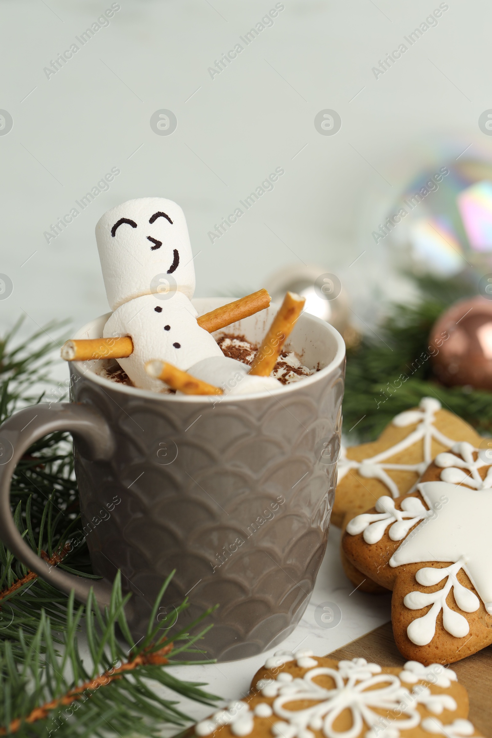 Photo of Cute marshmallow snowman in cup of hot drink and gingerbread cookies on table with Christmas decor