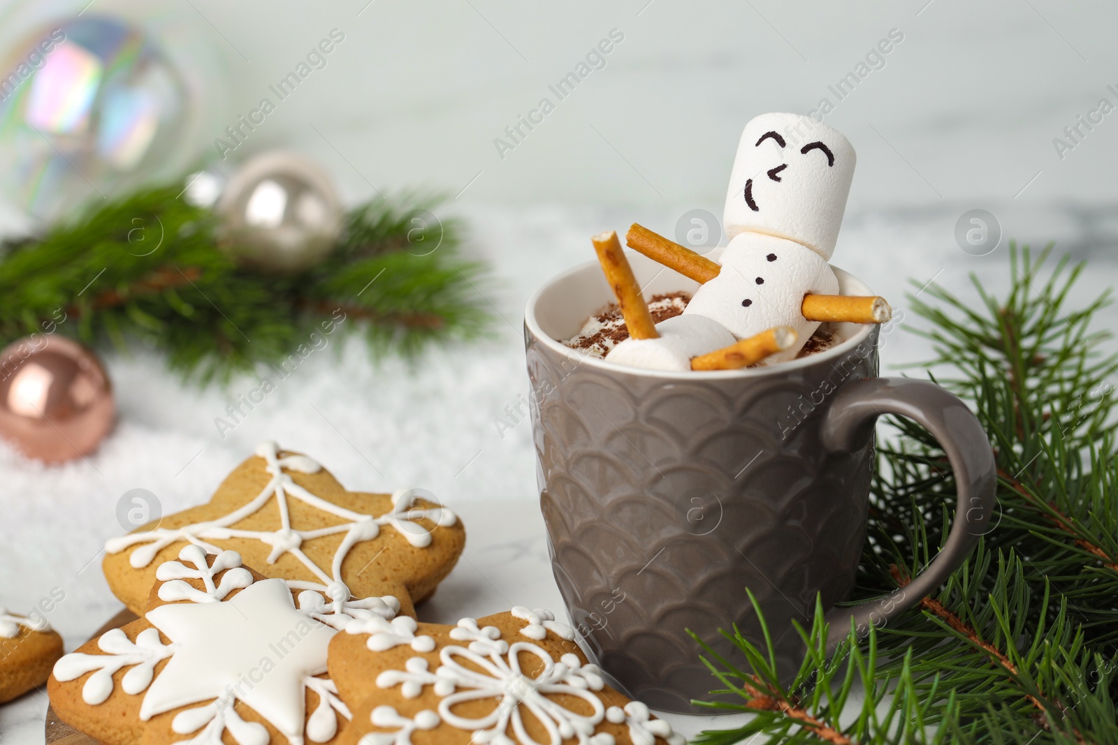 Photo of Cute marshmallow snowman in cup of hot drink and gingerbread cookies on white table with Christmas decor, closeup