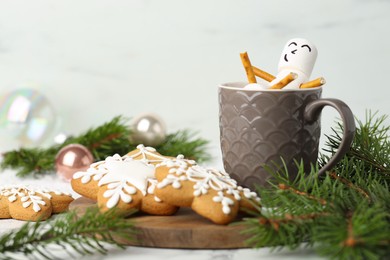 Photo of Cute marshmallow snowman in cup of hot drink and gingerbread cookies on white table with Christmas decor