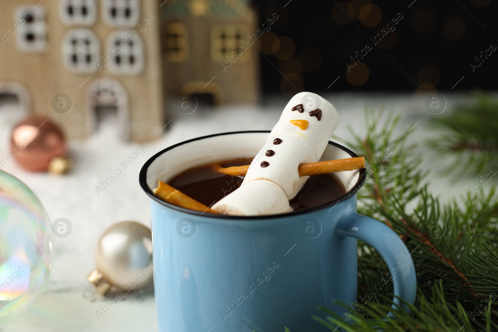 Photo of Cute marshmallow snowman in cup of hot drink on white table with Christmas decor, closeup