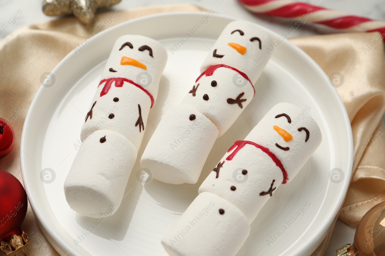 Photo of Funny marshmallow snowmen and festive decor on table, closeup