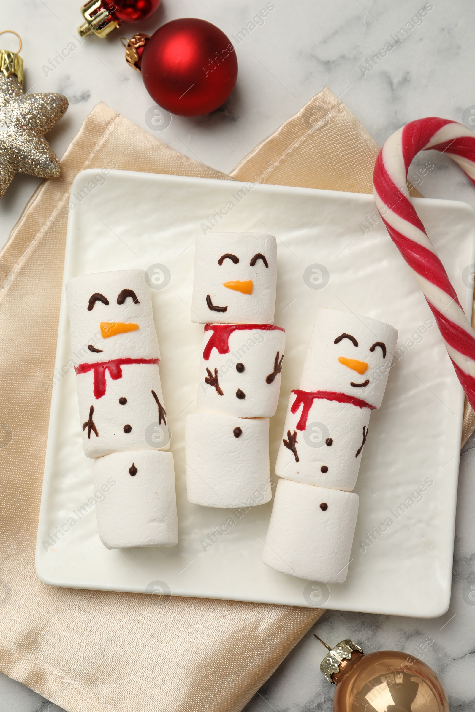 Photo of Funny marshmallow snowmen and festive decor on white marble table, top view