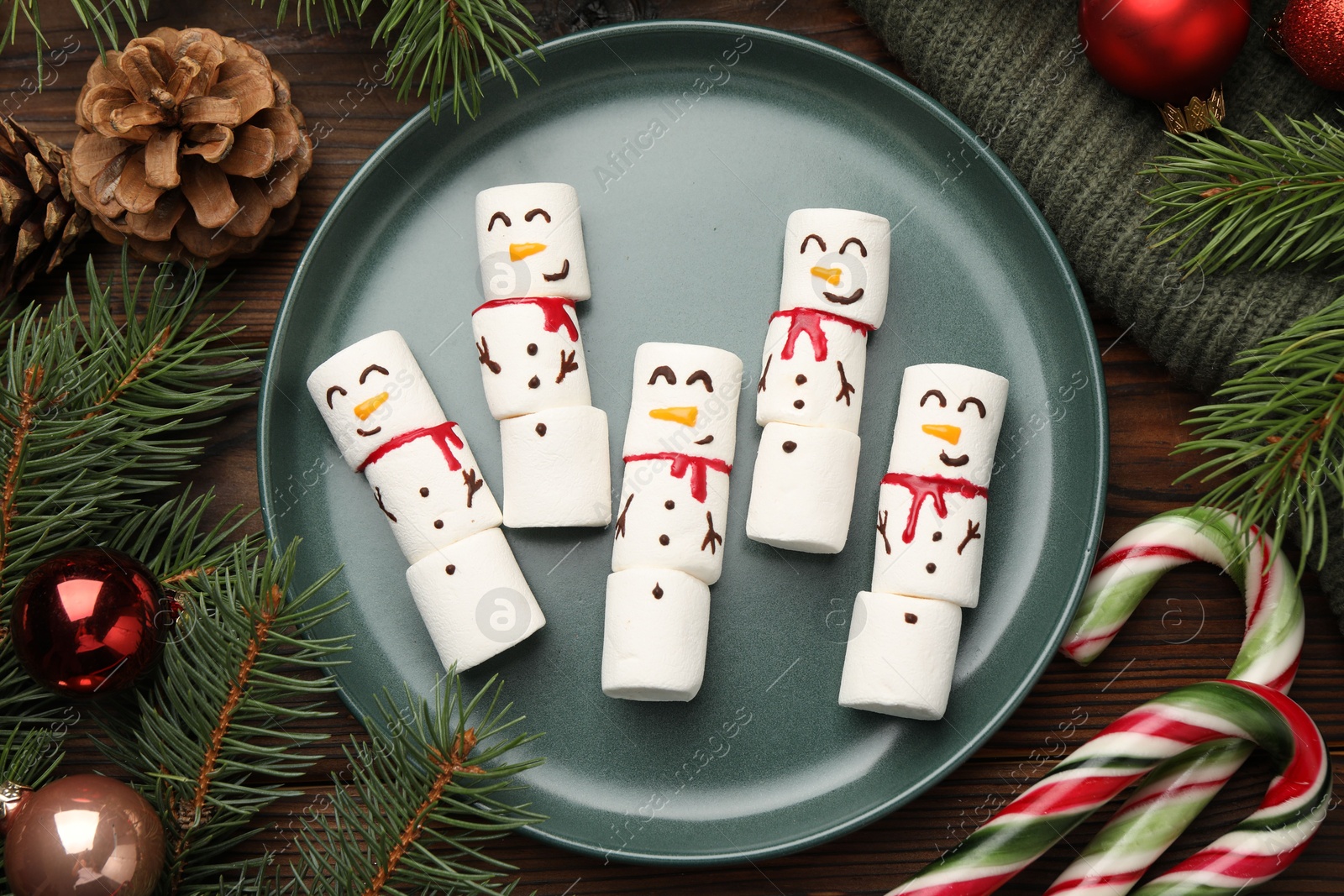 Photo of Funny marshmallow snowmen and festive decor on wooden table, flat lay