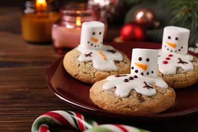 Funny marshmallow snowmen, cookies and festive decor on wooden table, closeup