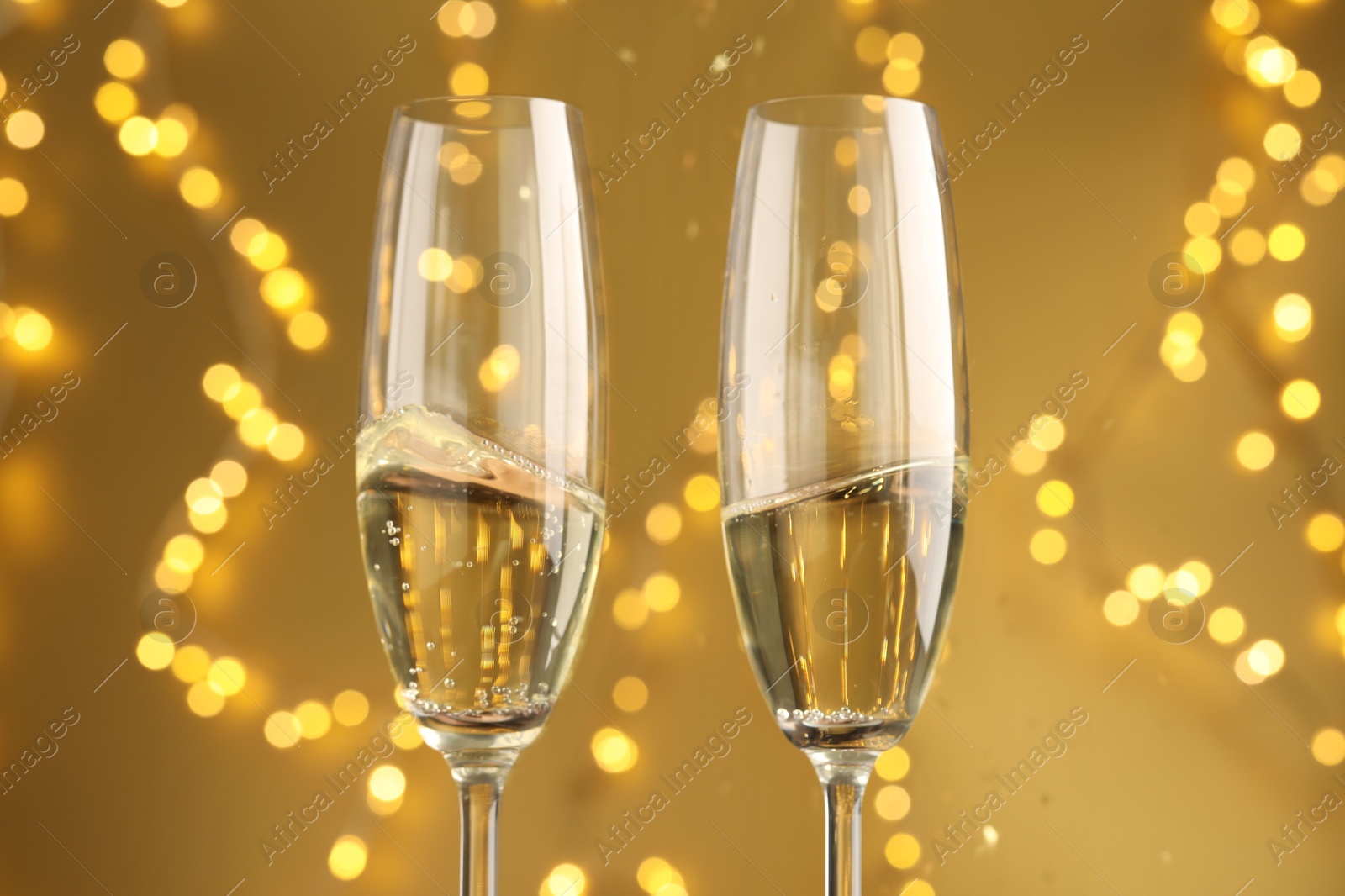 Photo of Glasses of sparkling wine against golden background with blurred lights, closeup. Christmas decor