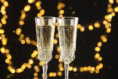 Photo of Glasses of sparkling wine and confetti against dark background with blurred lights, closeup. Christmas decor