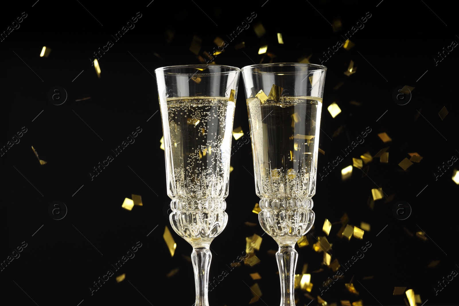 Photo of Glasses of sparkling wine and confetti against dark background, closeup. Christmas decor