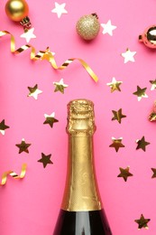 Photo of Bottle of sparkling wine, confetti and Christmas balls on pink background, flat lay