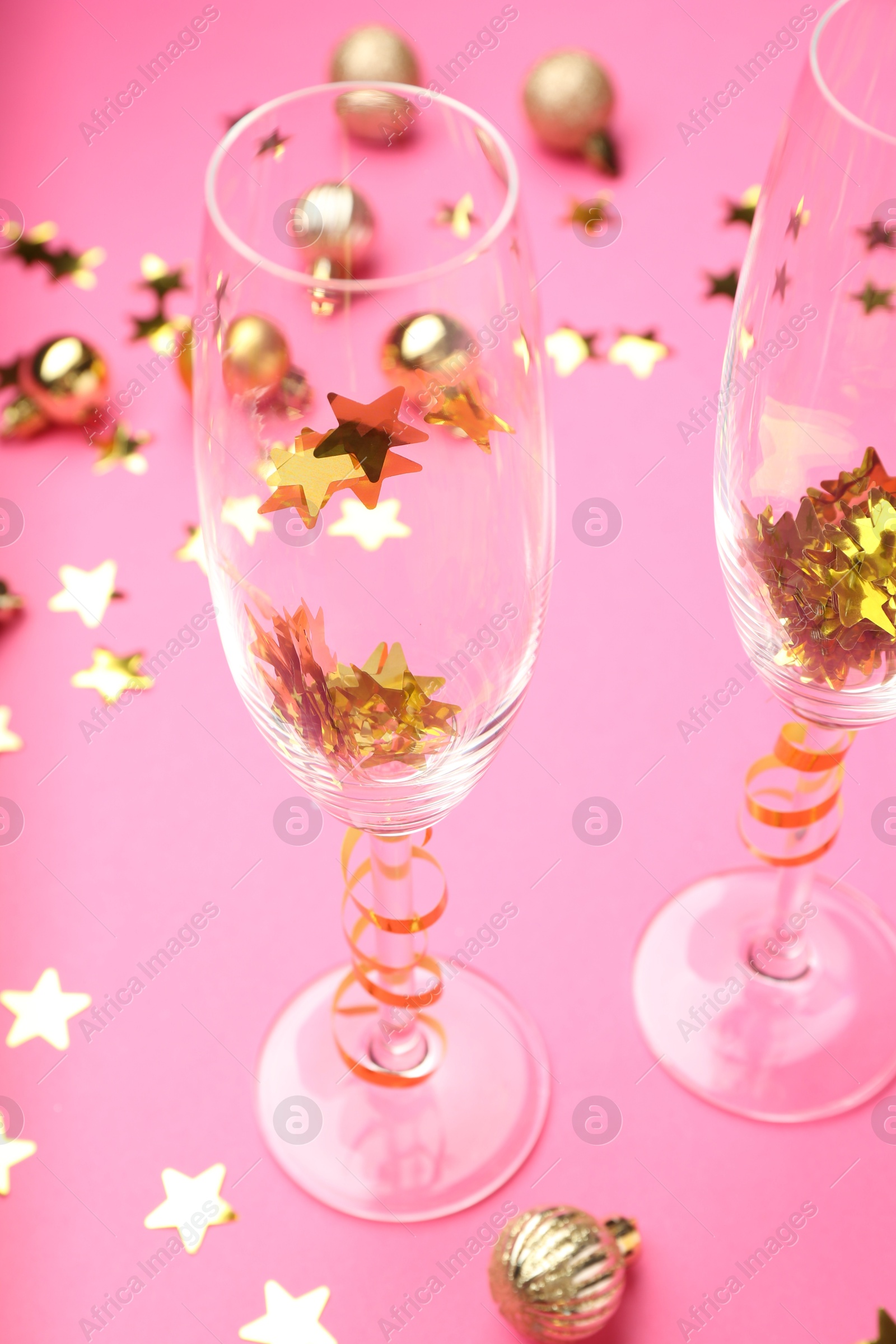 Photo of Wine glasses with confetti on pink background, closeup. Christmas decor