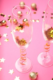 Photo of Wine glasses with confetti on pink background, closeup. Christmas decor