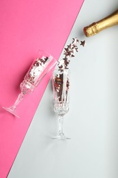 Photo of Glasses with confetti and bottle of sparkling wine on pink background, flat lay. Christmas decor