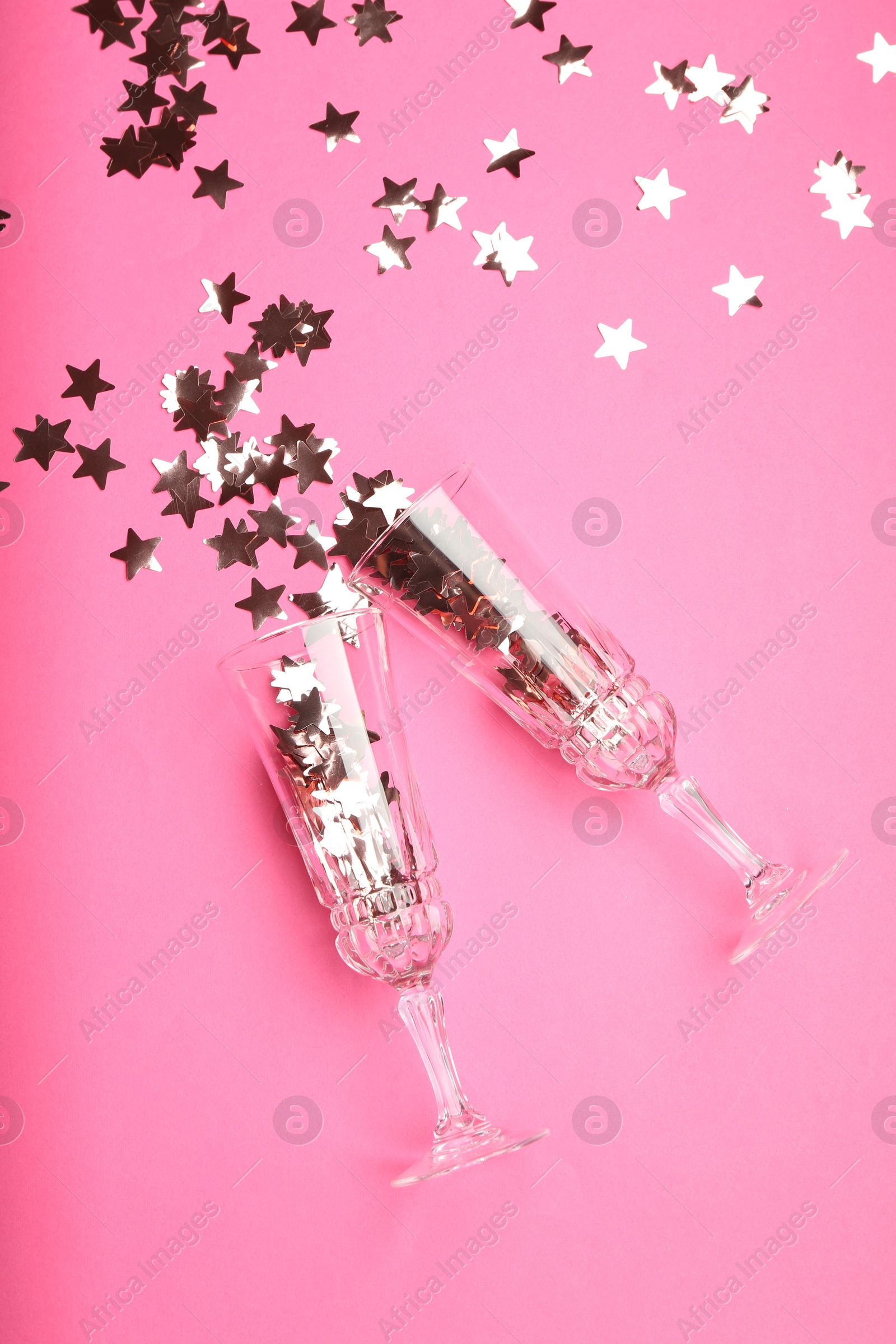 Photo of Wine glasses with confetti on pink background, flat lay. Christmas decor