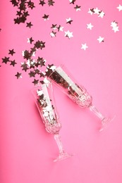 Photo of Wine glasses with confetti on pink background, flat lay. Christmas decor