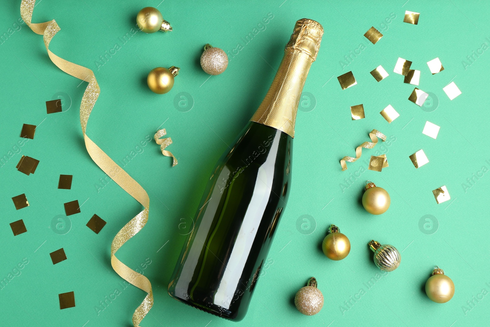 Photo of Bottle of sparkling wine, confetti and Christmas balls on green background, flat lay