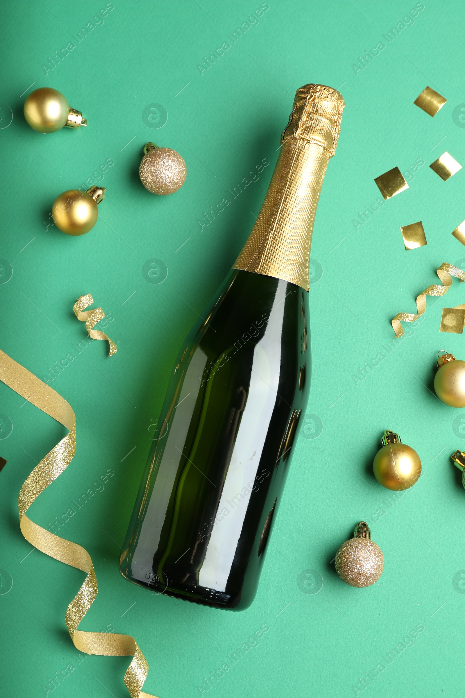 Photo of Bottle of sparkling wine, confetti and Christmas balls on green background, flat lay