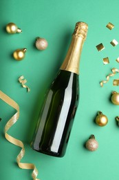 Photo of Bottle of sparkling wine, confetti and Christmas balls on green background, flat lay