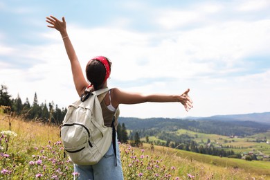 Photo of Tourist with backpack enjoying picturesque landscape with wide open arms, back view. Space for text