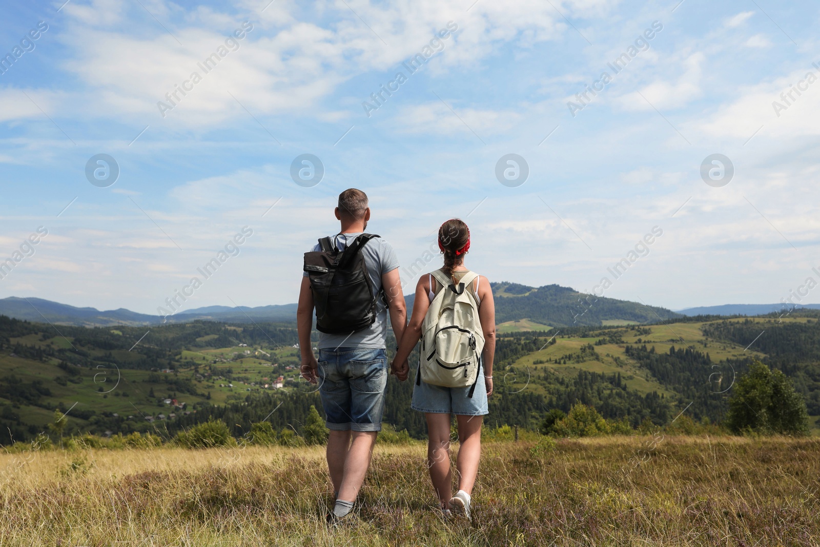 Photo of Couple with backpacks walking to mountains, back view. Active tourism