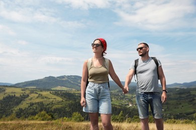 Photo of Happy couple with backpacks walking in mountains, space for text. Active tourism