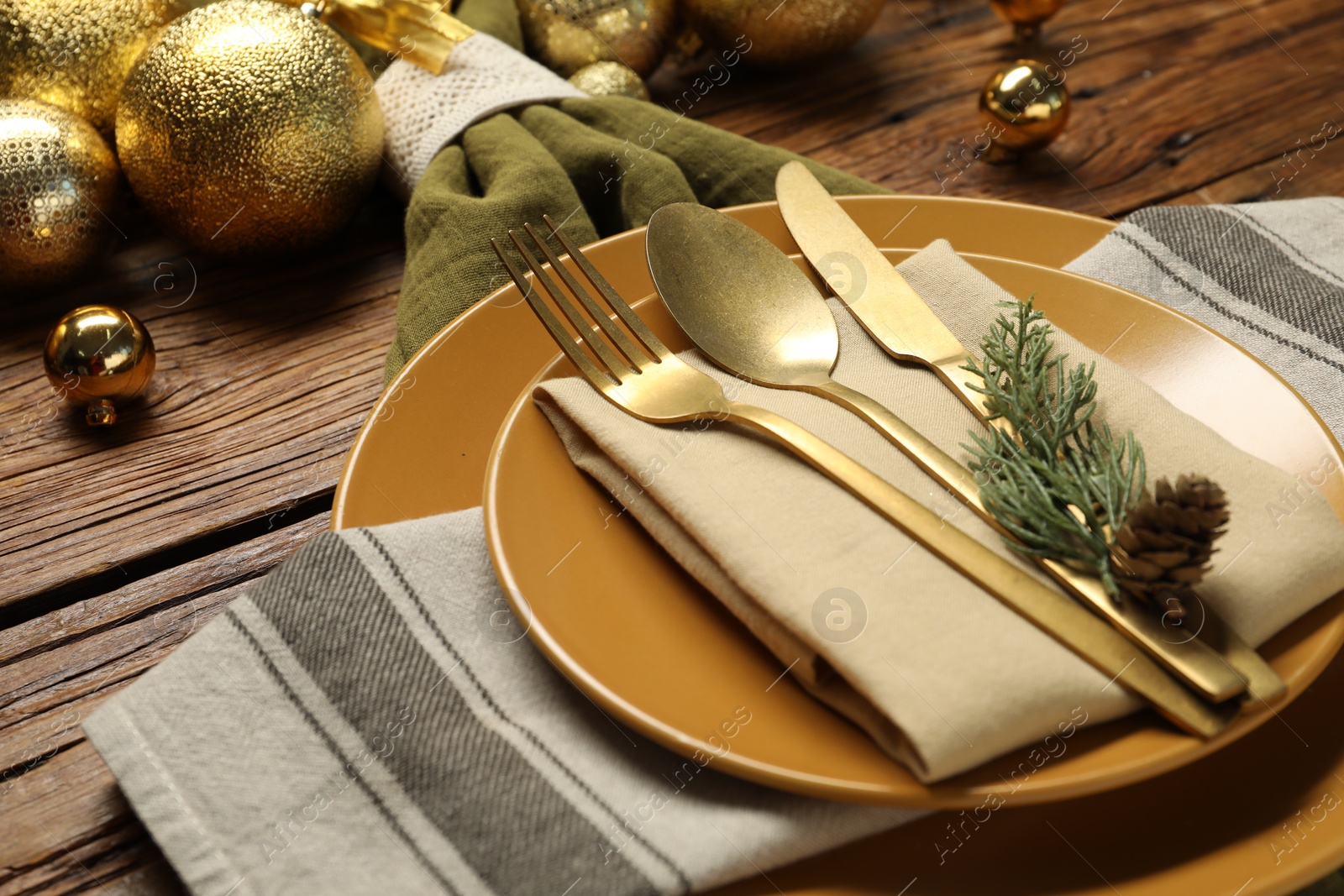 Photo of Christmas place setting with plates, cutlery and festive decor on wooden table, closeup