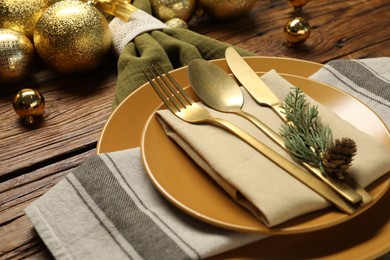 Photo of Christmas place setting with plates, cutlery and festive decor on wooden table, closeup