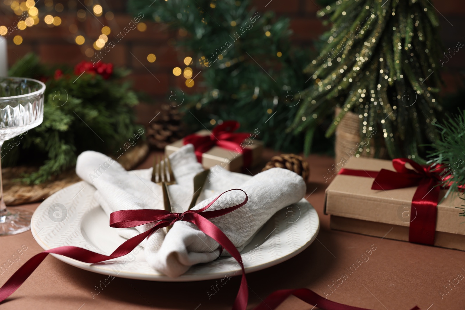 Photo of Christmas place setting with plate, napkin, cutlery and festive decor on brown table, closeup