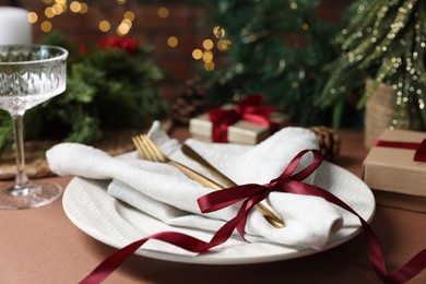 Photo of Christmas place setting with plate, napkin, cutlery and festive decor on brown table, closeup