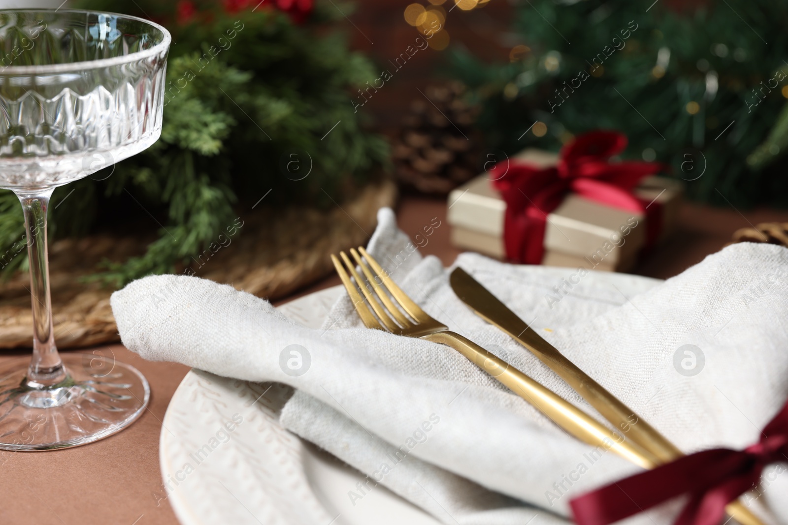 Photo of Christmas place setting with plate, napkin, glass and cutlery on brown table, closeup