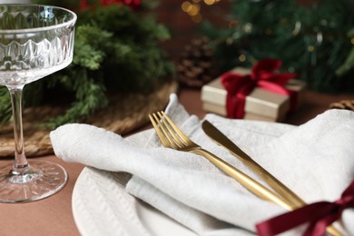 Photo of Christmas place setting with plate, napkin, glass and cutlery on brown table, closeup