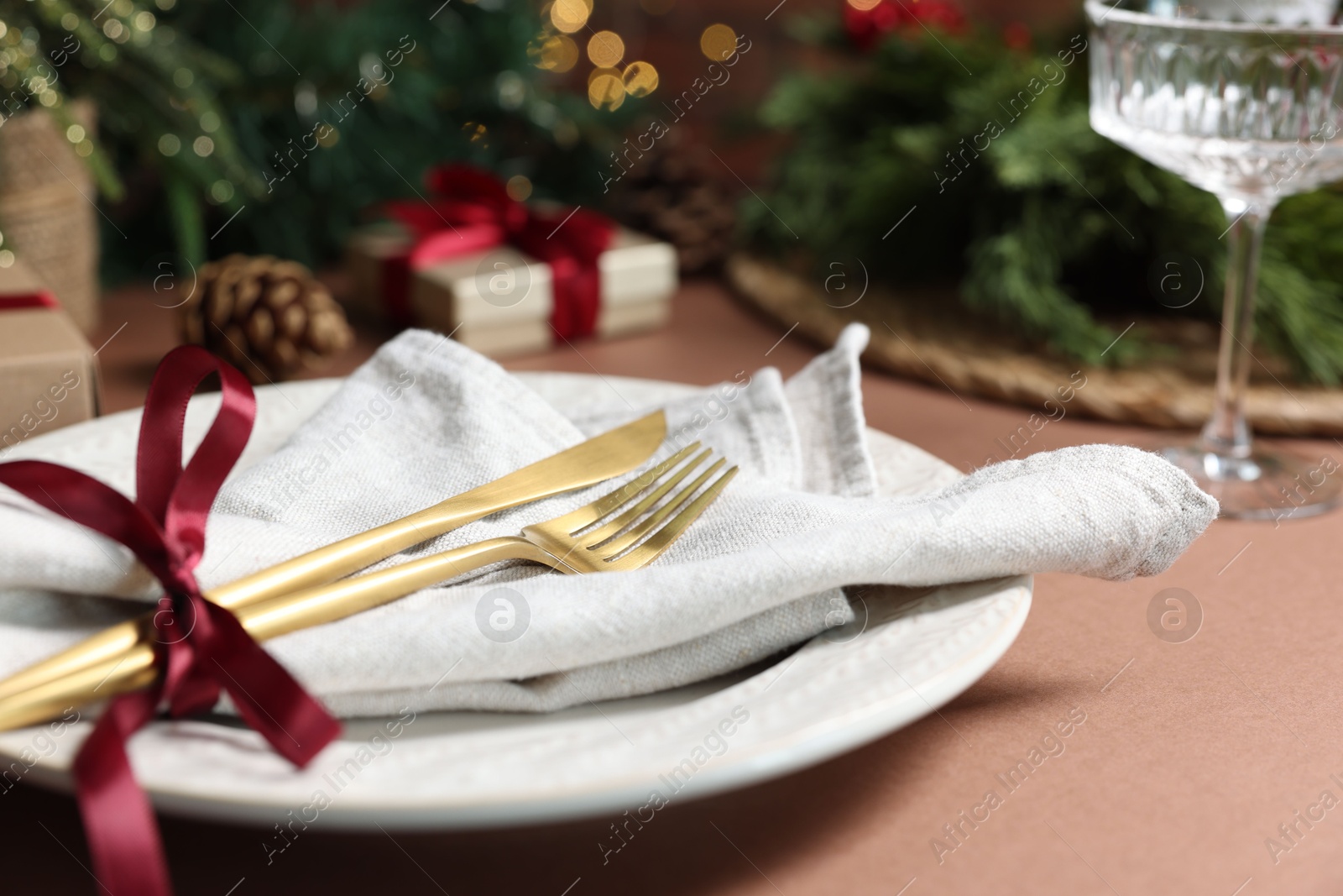 Photo of Christmas place setting with plate, napkin and cutlery on brown table, closeup