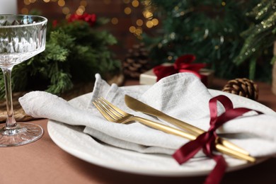 Photo of Christmas place setting with plate, napkin, cutlery and festive decor on brown table, closeup