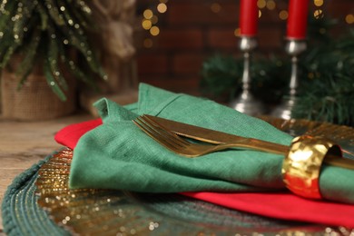 Photo of Christmas place setting with napkin, cutlery and festive decor on wooden table, closeup