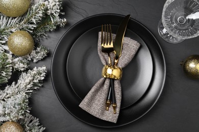 Photo of Christmas place setting with plates, cutlery, glass and festive decor on black table, top view