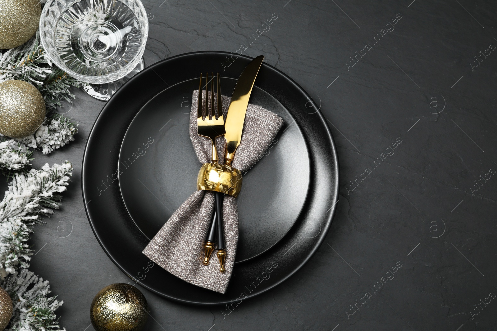 Photo of Christmas place setting with plates, cutlery, glass and festive decor on black table, top view