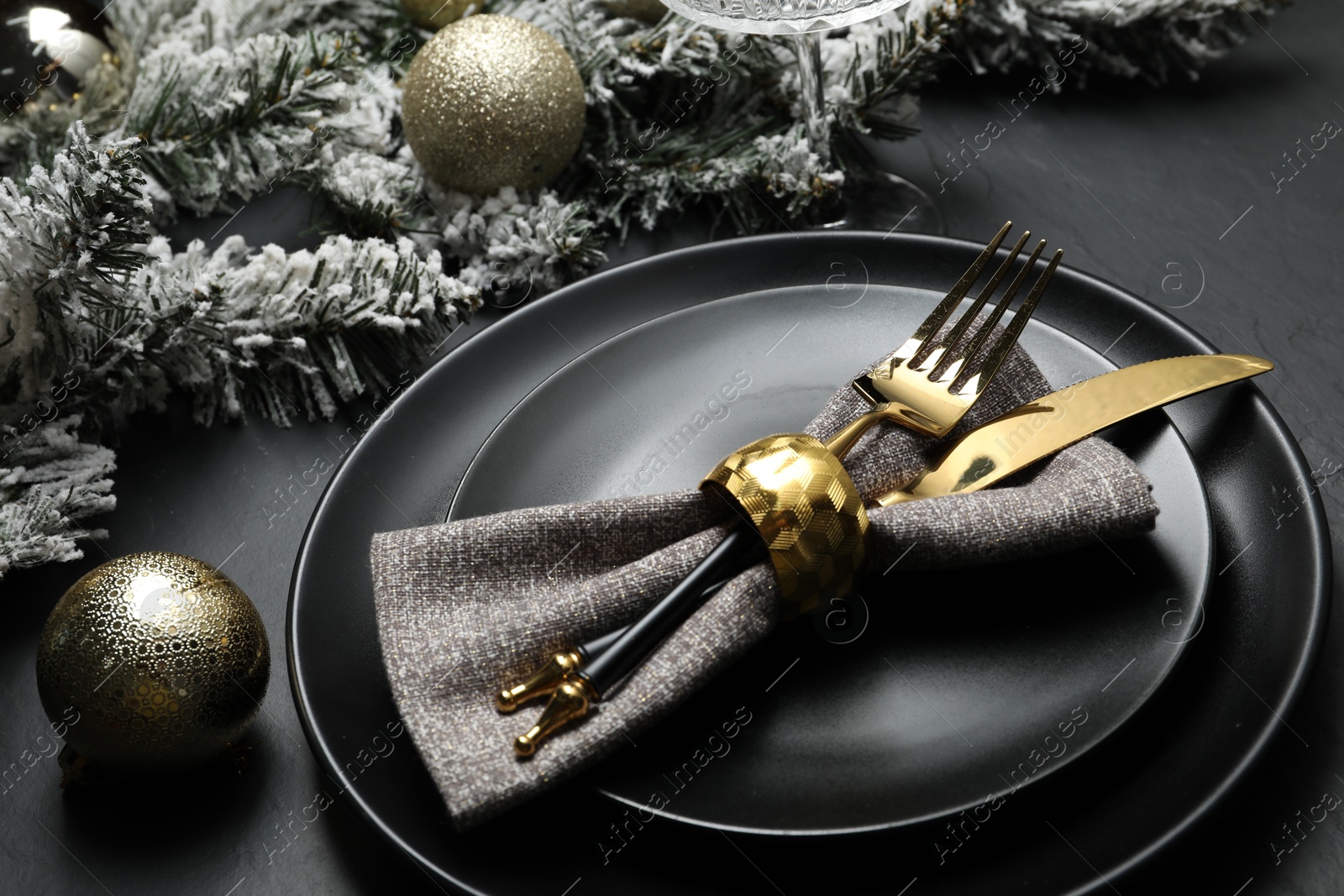 Photo of Plates, cutlery and Christmas decor on black table, closeup