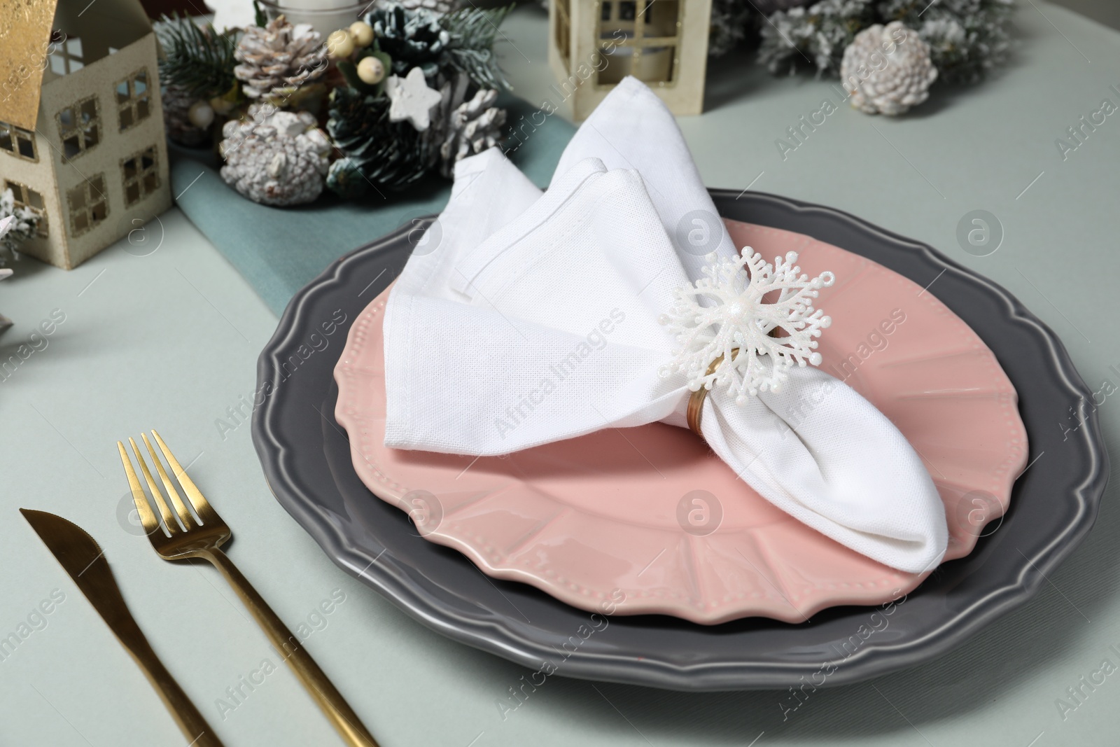 Photo of Christmas table setting with plates, cutlery and festive decor on light grey background, closeup