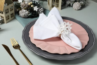 Photo of Christmas table setting with plates, cutlery and festive decor on light grey background, closeup