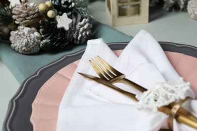 Photo of Christmas table setting with plates, cutlery and festive decor on light grey background, closeup